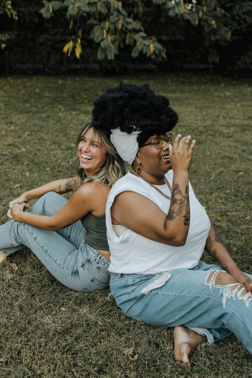 a couple of women sitting on top of a grass covered field