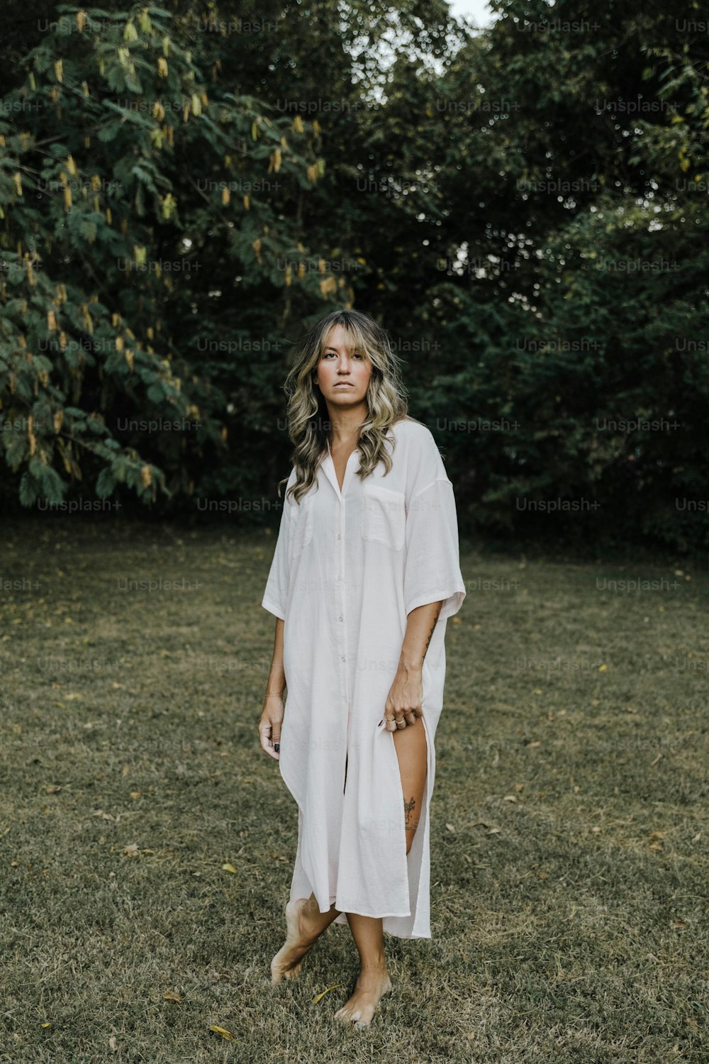 Une femme debout dans un champ vêtue d’une robe chemise blanche