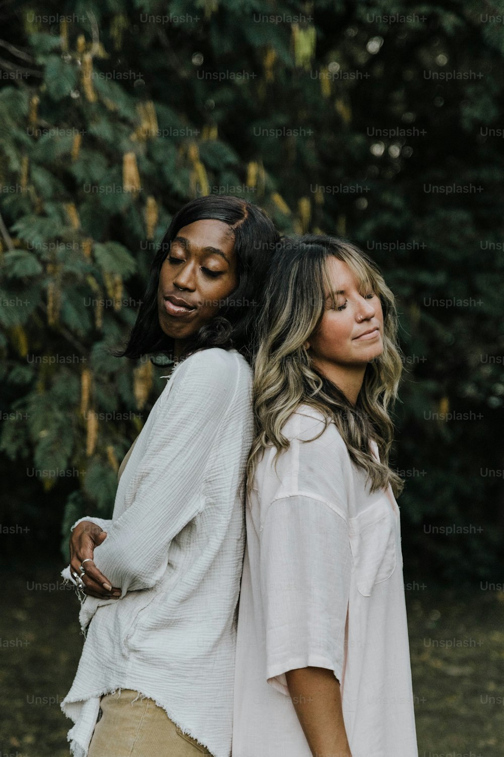 two women standing next to each other in front of trees