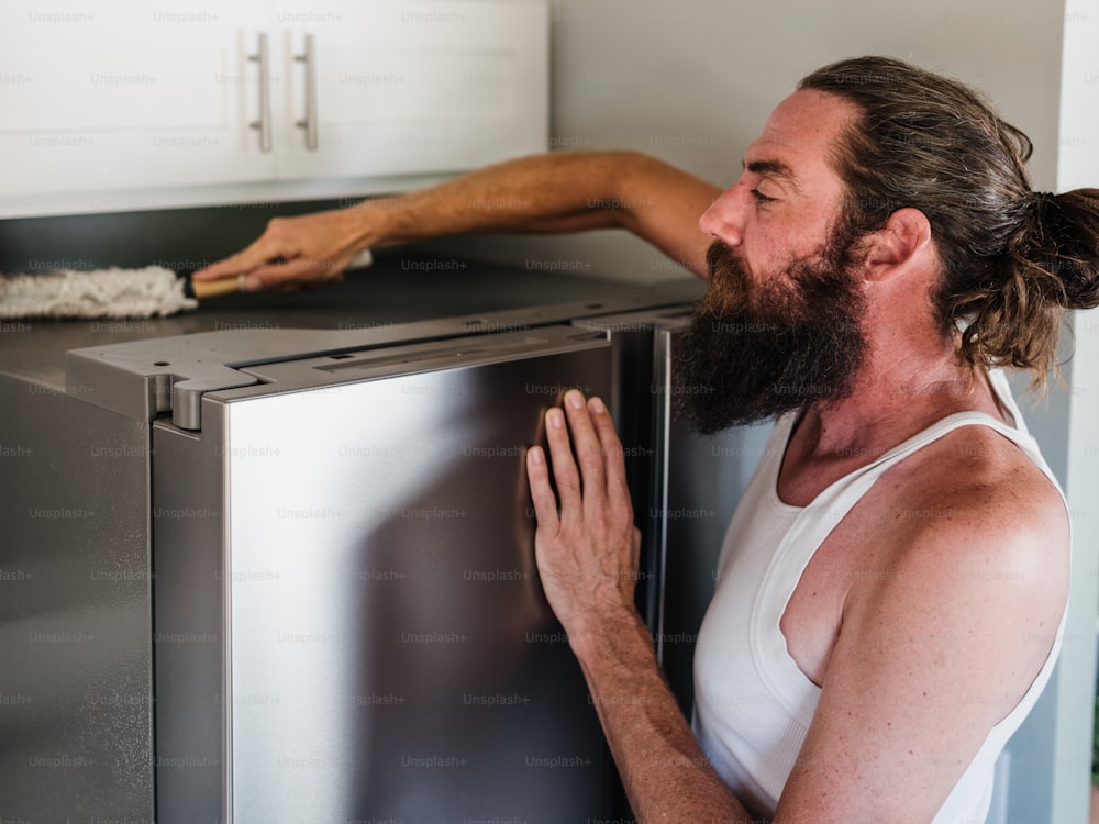 Um homem com barba está encostado em uma geladeira