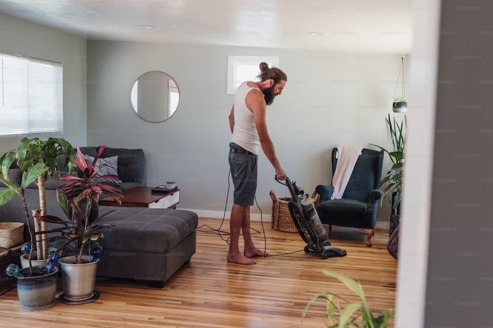 リビングルームの堅い木の床を掃除機で掃除する男