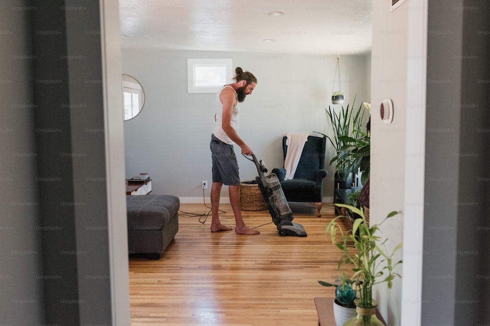 거실에서 딱딱한 나무 바닥을 진공 청소기로 청소하는 남자