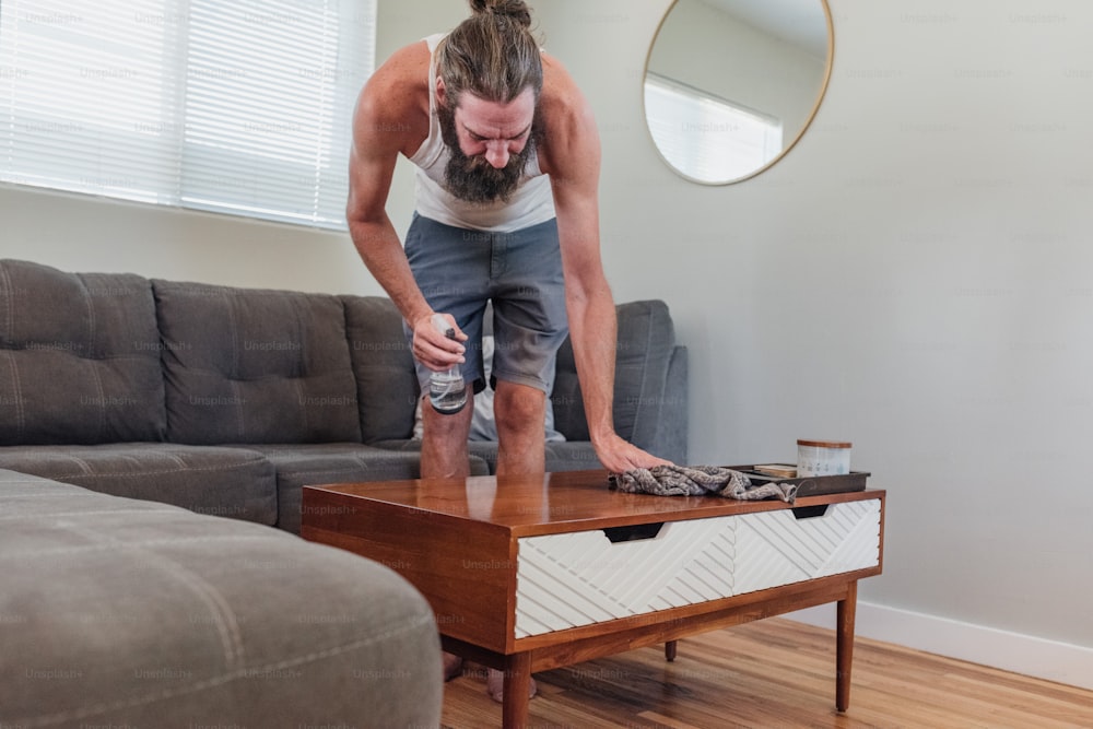 a man standing over a coffee table with a bottle of water