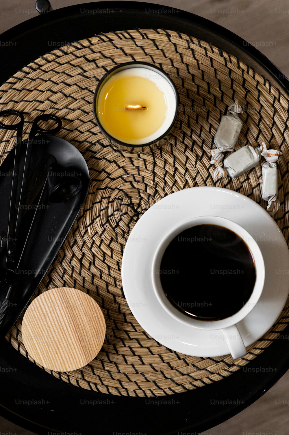 una taza de café, cucharas y una vela en una bandeja de mimbre