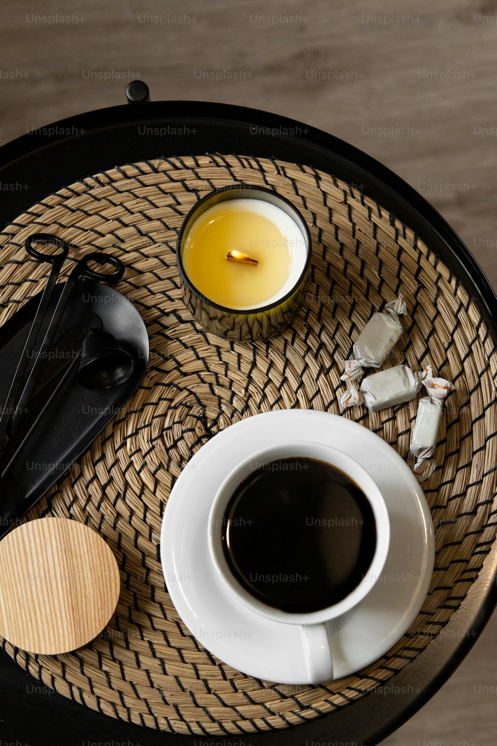 a cup of coffee, spoons, and a candle on a wicker tray