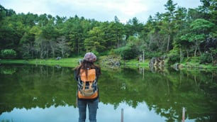 若い女性は自然を旅します。彼女は公園の水辺に立って美しい風景を撮影しています。