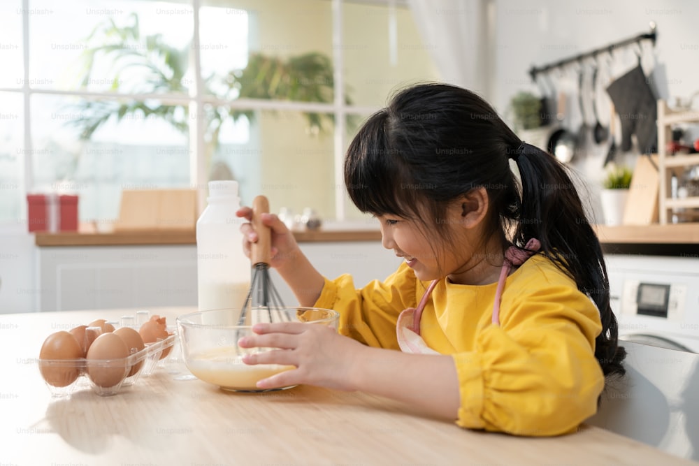 Portrait d’une jeune fille asiatique mignonne faisant de la boulangerie maison dans la cuisine. Adorable petit enfant assis sur la table se sentant heureux et s’amuse à apprendre à cuisiner des aliments ou à cuire pétrit de la pâte à levure avec les mains à la maison