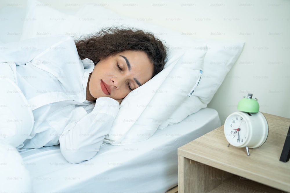 Latino beautiful woman lying down on bed in bedroom in early morning. Attractive young female in pajamas sleeping alone on comfortable pillow and cozy blanket in bright room for health care at home.