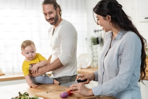 Caucasian family, Mother cook foods with dad and baby son in kitchen. Loving Father carry little young toddler kid child, have fun spend time together with mom in house. Activity relationship concept.