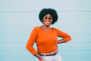 Portrait of cheerful Afro American girl smiling and looking at the camera. Happiness concept. Afro woman with orange sweater in front of green wall.