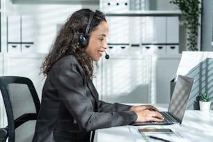 라틴계 아름다운 비즈니스 여성 콜센터 미소는 사무실에서 일하는 동안. 정장을 입은 매력적인 젊은 여성 직원 직원이 직장에서 테이블에 앉아 노트북 컴퓨터 대화를 사용하여 고객을 지원합니다.