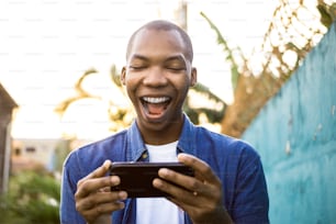 jovem negro africano segurando seu telefone.rindo exageradamente. conceito de felicidade.