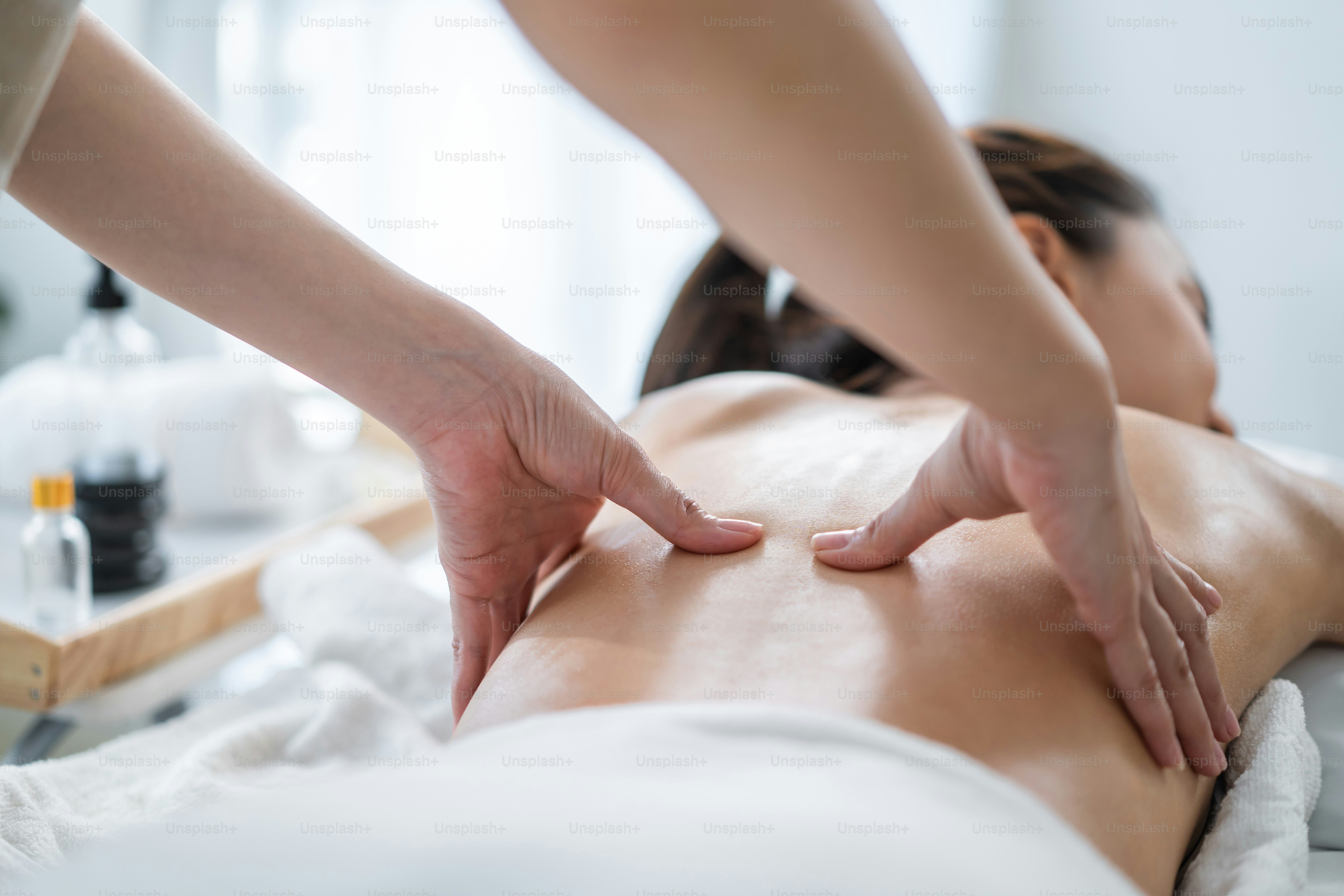 Asiatische junge Frau fühlt sich glücklich und entspannt sich bei der Rückenmassage mit Öl. Attraktives schönes Mädchen liegt auf dem Massagetisch und bekommt Physiotherapie von Masseurin für Haut- und Körperpflege im Spa-Schönheitssalon