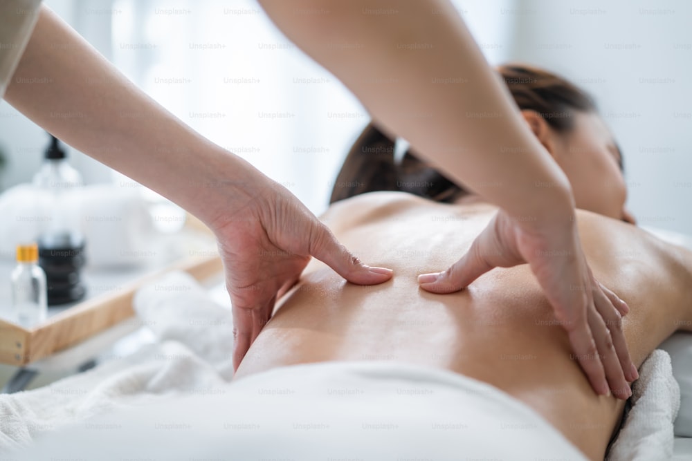 Asian young woman feeling happy and relax during back massage with oil. Attractive beautiful girl lying on massage table, getting physiotherapy from masseuse for skin and body care in spa beauty salon