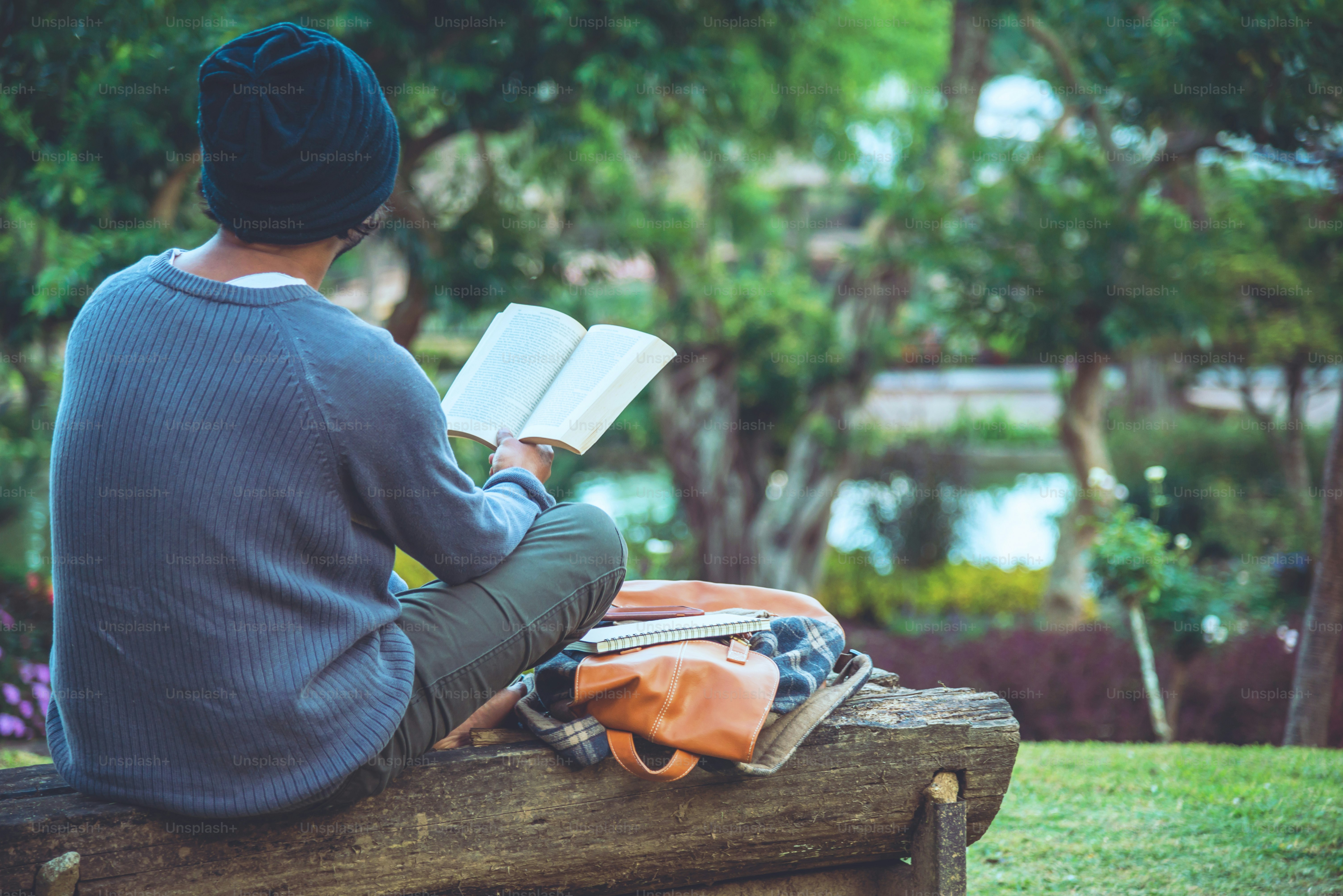 Il giovane stava leggendo un libro al parco. Tra gli alberi spontanei e il bellissimo giardino fiorito