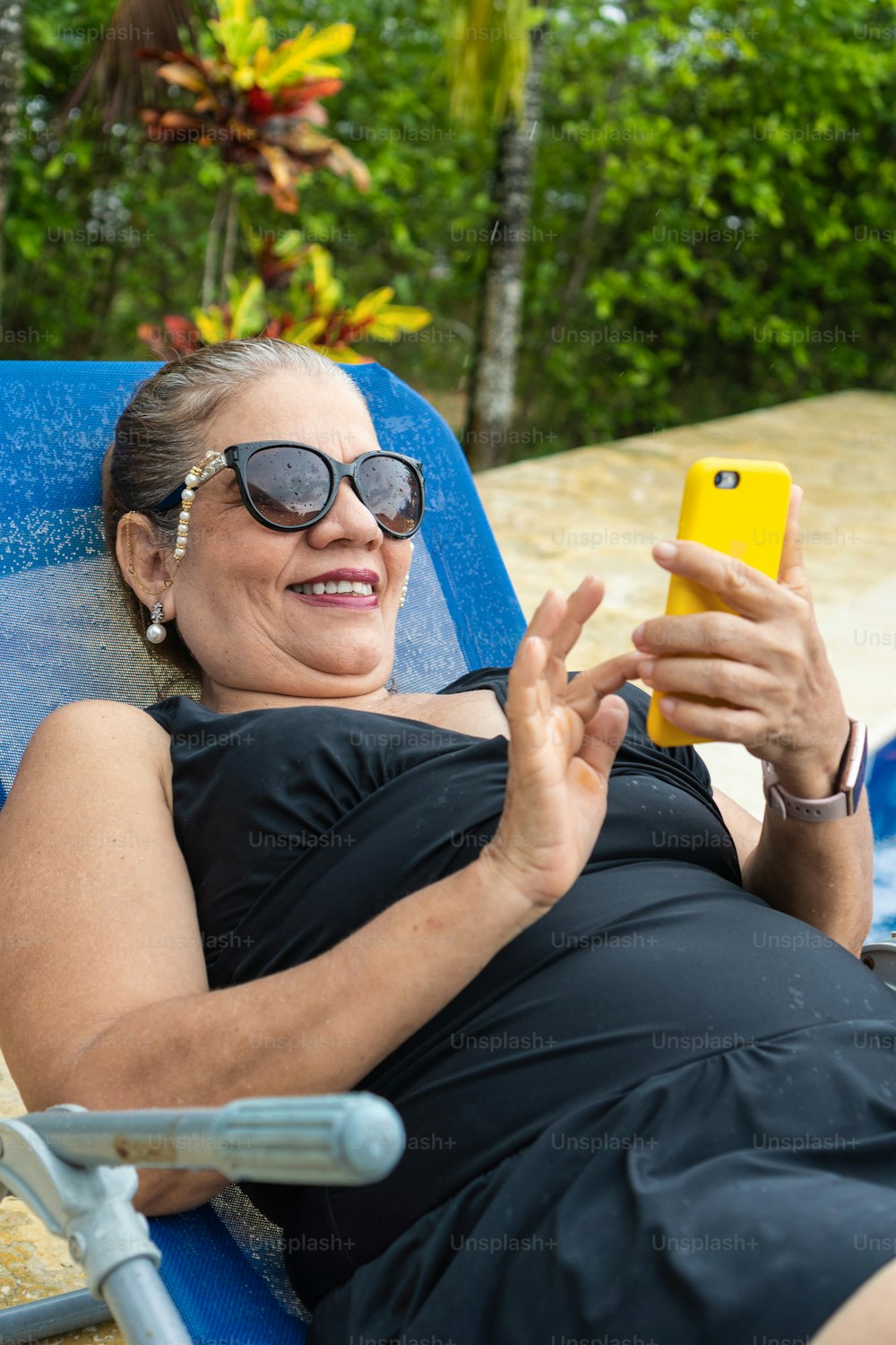 Hispanic woman sitting poolside and checking smartphone.