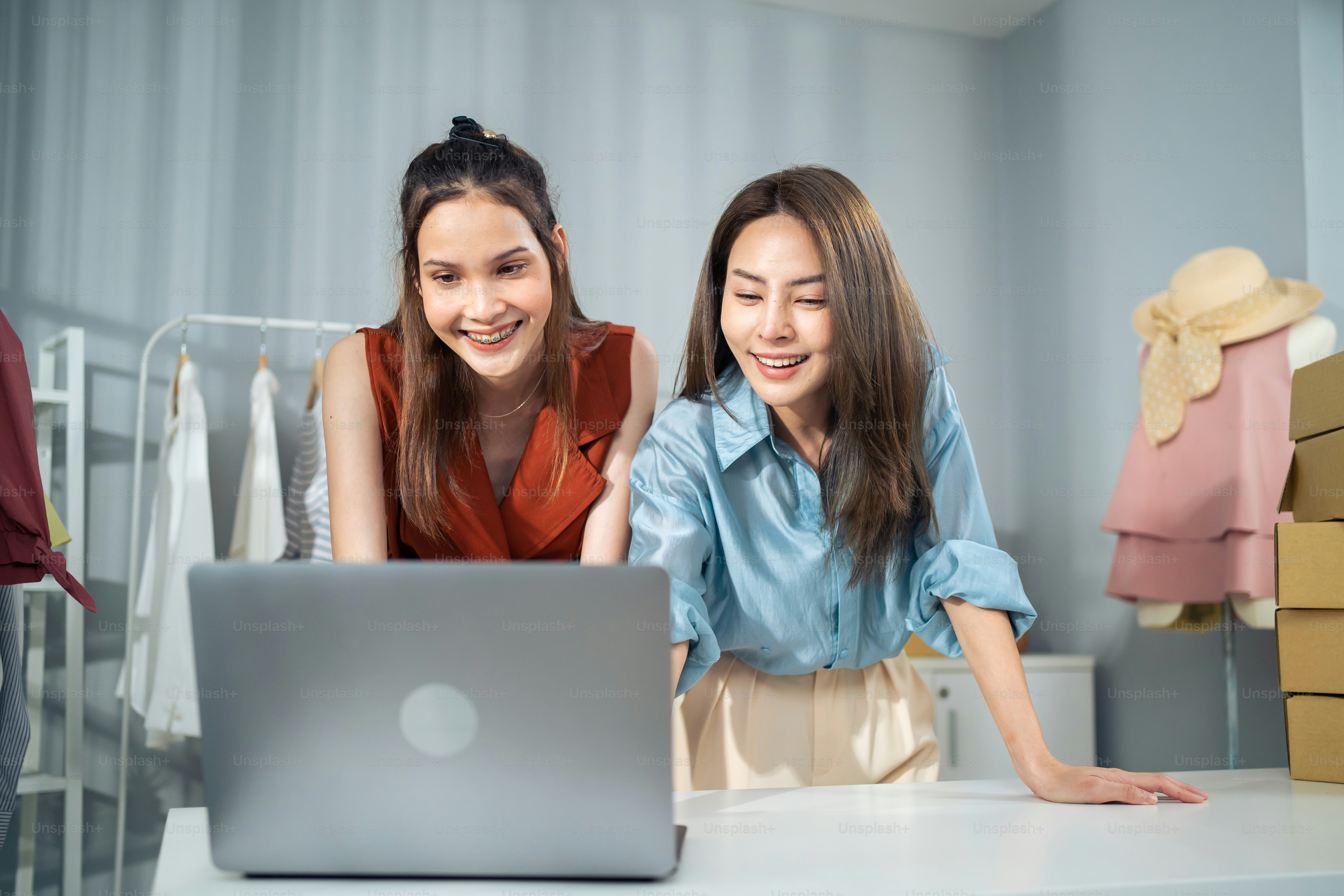 Asian woman friends couple packing clothes order into box for customer. Young attractive business people work to preparing parcel boxes check ecommerce shipping online retail to sell at office store.