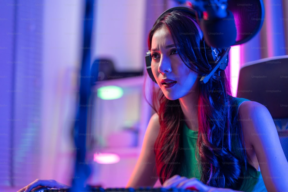 アジアの美しいeスポーツの女性ゲーマーは、コンピューターでオンラインビデオゲームをプレイします。魅力的な若い女の子のゲームプレーヤーは、自宅でサイバートーナメントをプレイしながら、幸せを感じ、テクノロジー放送のライブストリーミングを楽しんでいます