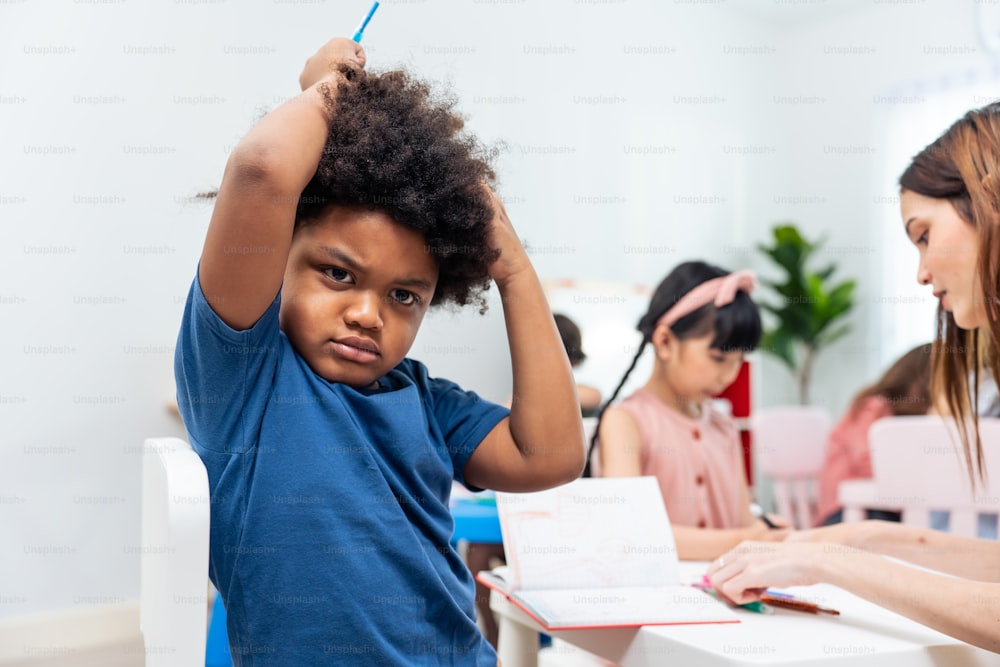 Retrato de niño negro africano estresado sentado en el aula. Estudiante deprimido, niño pequeño, niño pequeño que se siente cansado y preocupado mientras estudia arte y dibujo en el aula y mira a la cámara en la escuela