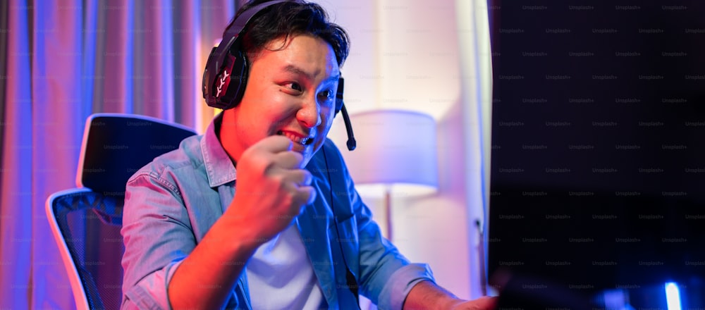 아시아의 매력적인 Esport 남성 게이머는 컴퓨터에서 온라인 비디오 게임을합니다. 잘 생긴 남자 게임 플레이어는 행복하고 흥분을 느끼고, 집에서 사이버 토너먼트를하는 동안 기술 방송 라이브 스트리밍을 즐깁니다.