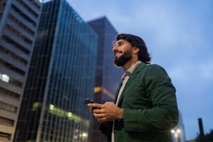 View of young man using a smartphone at night time with city view landscape in the background. Mobile phone, technology, urban concept. High quality photo