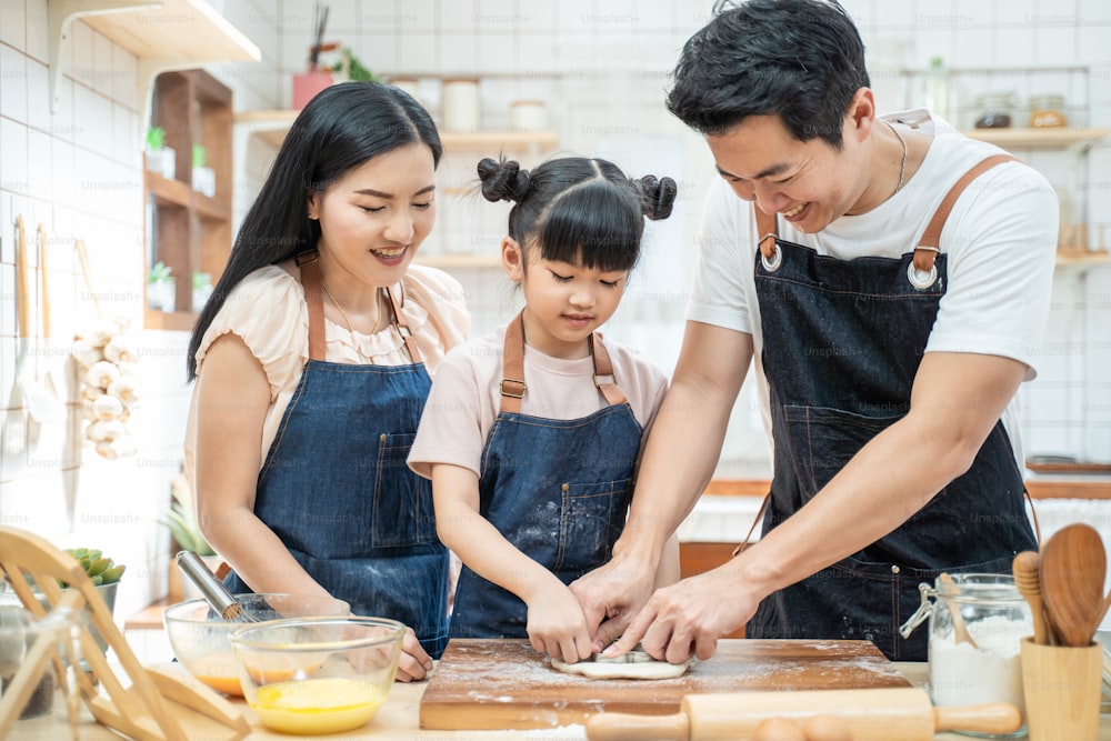 Asiatische glückliche Familie bleiben zu Hause in der Küche und verbringen Zeit zusammen Backen Bäckerei und Lebensmittel. Kleines Vorschulkind, das von Eltern, Vater und Mutter lernt, genießt die elterliche Aktivität Beziehung im Haus.