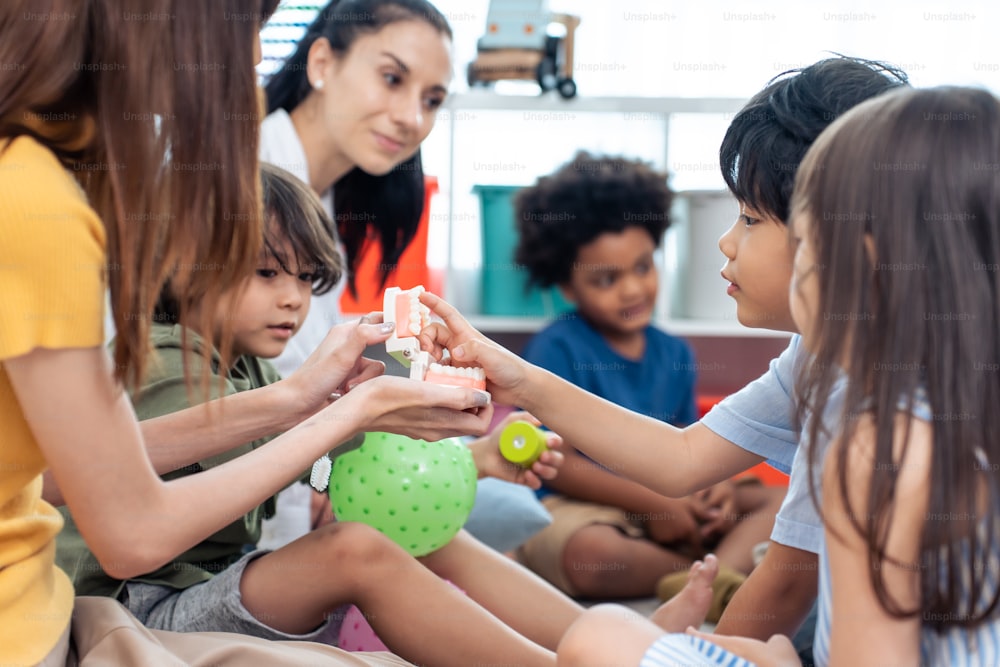 Asian beautiful young woman teacher teaching mixed race kids at school. Attractive women instructor master explain and educate children student with fun activity in classroom at preschool kindergarten