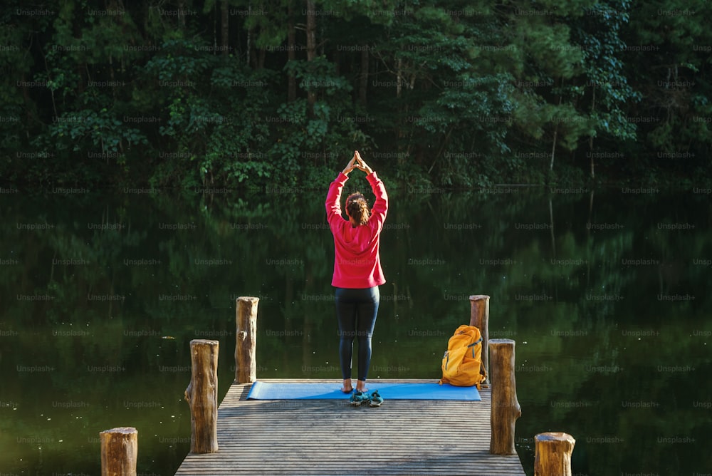 Las mujeres asiáticas se relajan en las vacaciones. Juega al yoga. En el Moutain, ejercicio, juega al yoga en el puente de bambú junto al lago en la niebla en Pang Ung, Tailandia.