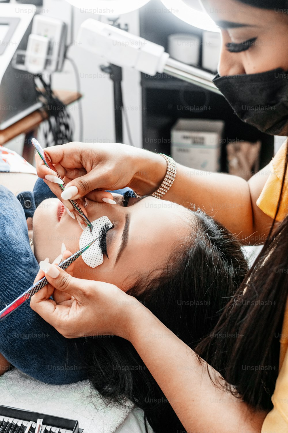 Hands holding tweezers while performing eyelash extension attachment.