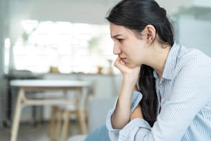 Asian beautiful unhappy woman sit on sofa feel frustrated and stressed. Attractive worried female having psychological problem feeling anxiety depression, upset and grief troubled for health at home.