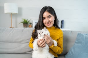 Retrato de una mujer hermosa sosteniendo un gatito con felicidad en casa. Atractiva mujer sentada en el sofá, pasando el tiempo libre de ocio con su animal mascota en la sala de estar y mirando a la cámara en la casa.