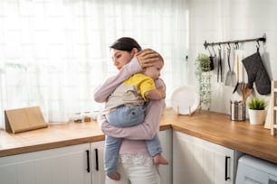 La madre amorevole caucasica tiene in braccio il bambino per cullarlo nel sonno. La mamma attraente porta il figlio del bambino con delicatezza e tenerezza per un sano pisolino diurno in casa. Concetto di maternità-genitorialità.