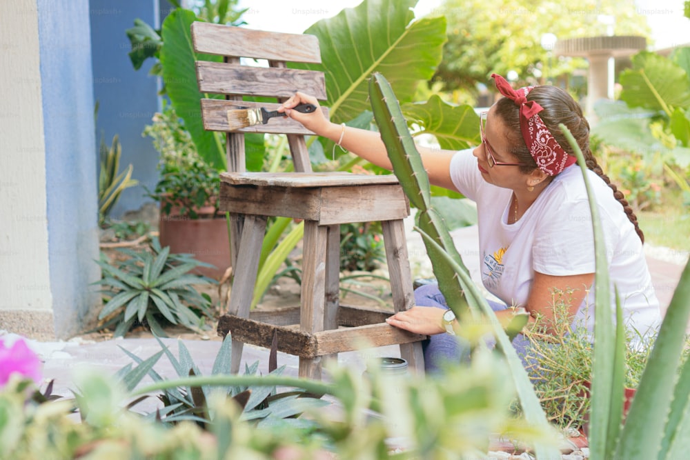 Young woman painting wooden chairs in garden