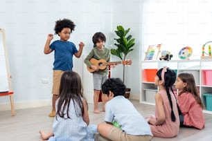 Group of Mixed race young little kid playing guitar in schoolroom. Child girl and boy student  spend time play music sing a song and dancing while break with feeling fun together in classroom at schoo