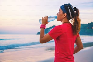 Asian women jogging workout on the beach in the morning. Relax with the sea walk and drinking water from the plastic bottles