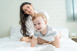 Portrait of Caucasian happy family smiling, look at camera in bedroom. Young attractive woman parents, mother in pajamas laying on bed with little baby boy child enjoy morning wake up activity at home