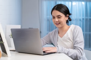 Asian young woman study virtual online and work in living room at home. Distance learning of beautiful Business girl typing on laptop computer at night time in house. Homeschool late of work concept.