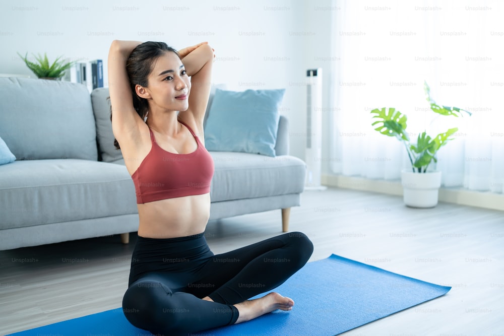 Asian young beautiful active woman doing Yoga Pilates workout at home. Attractive girl in sportswear feel happy and relax, follow exercise instruction video from online trainer in living room in house