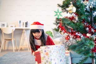 Asian young little daughter open present gift box under Christmas tree. Happy family, little kid feel happy and excited for surprise from mother and father ready to celebrate Xmas together in house.