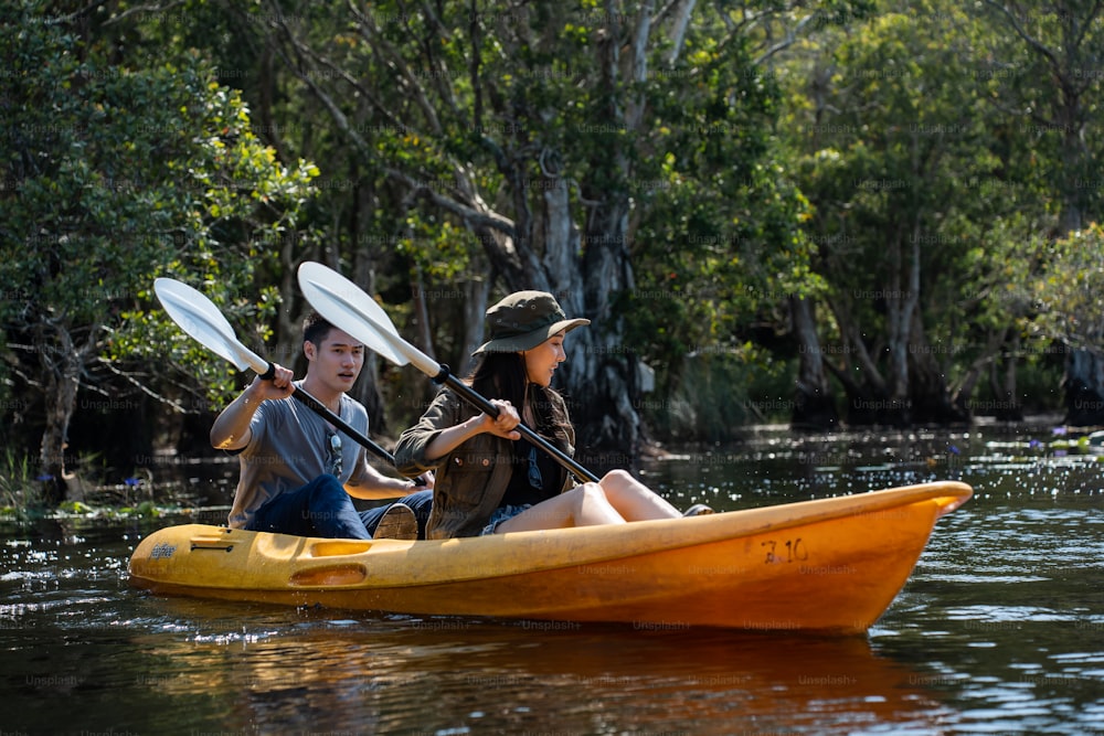 Asian attractive romantic young couple rowing kayak in a forest lake. Backpacker man and woman travel and kayaking on canoe in beautiful mangrove forest enjoy spend time on holiday vacation together.