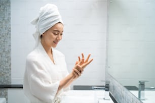 Asian beautiful woman putting smooth and soft skin care on hands. Attractive female touches on face and applying cream lotion for rejuvenation with gentle after shower. Beauty, skincare and healthcare