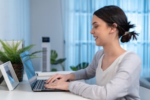 Asian young woman study virtual online and work in living room at home. Distance learning of beautiful Business girl typing on laptop computer at night time in house. Homeschool late of work concept.