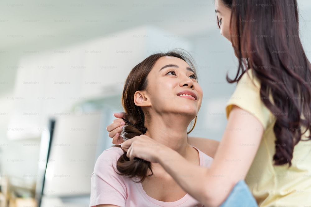 Asian beautiful lesbian women couple combing girlfriends hair in house. Attractive two female gay friend sit on sofa in living room, feel happy for beauty cosmetic together. Homosexual-LGBTQ concept.