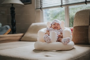 Happy laughing and smiling Asian baby girl sitting in Inflatable baby seat on sofa at home in morning sunlight
