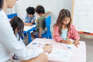 Caucasian beautiful woman teacher teaching a lesson to kid at school. Attractive female instructor master explain and educate children student with fun activity in classroom at preschool kindergarten.