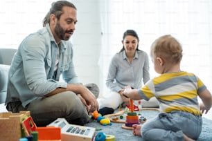 Caucasian happy loving parent play with baby toddler in living room. Attractive couple mother and father spend time with young little infant son child in house. Activity relationship at home concept.