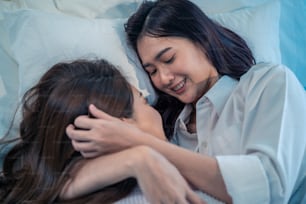 Asian beautiful lesbian couple lying down on bed and hugging each other. Attractive romantic girl friend in pajamas spending night leisure time together in bedroom. Homosexual freedom pride concept.