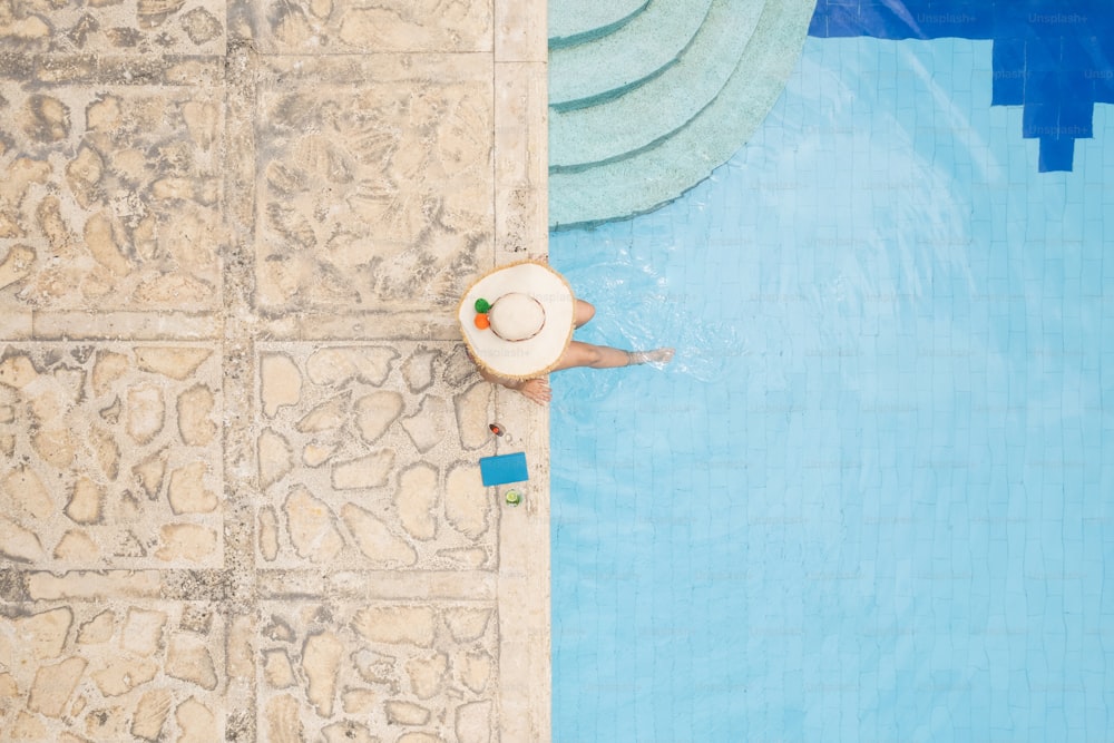 Vista aérea de la mujer con sombrero para el sol relajándose, tomando el sol en la piscina de verano