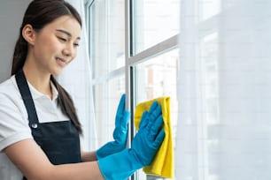 Asian cleaning service woman worker cleaning in living room at home. Beautiful happy girl housewife housekeeper cleaner wear apron and vacuuming messy dirty curtain for housekeeping housework or chore