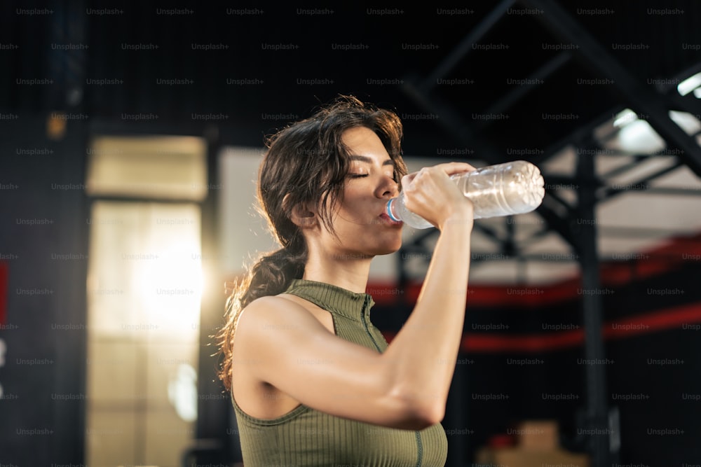 Latino young sport girl athlete in sportswear drinking in fitness gym. Active fitness female standing and resting after finished work out from lifting up machine for health care in fitness gym stadium
